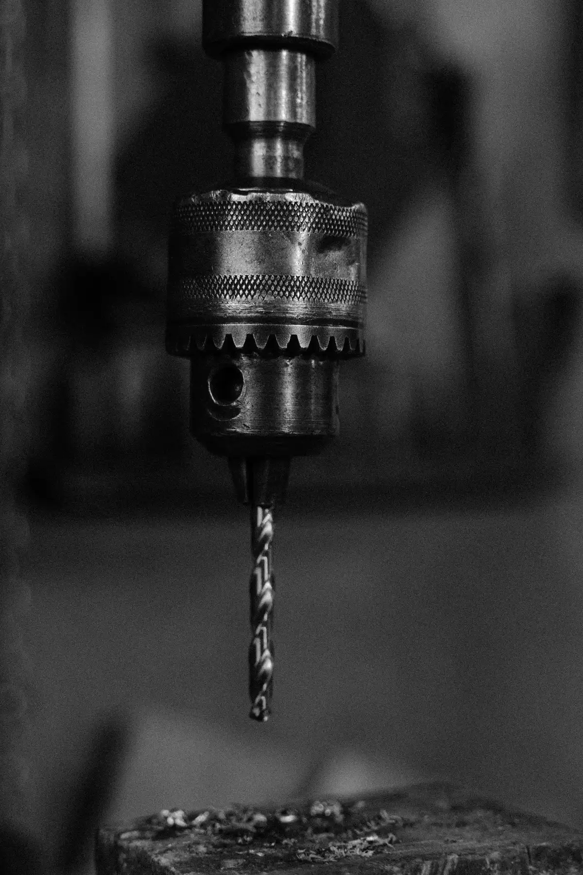 Close-up of a keyed drill chuck and twist bit, knurled collar sharp against a dark workshop.