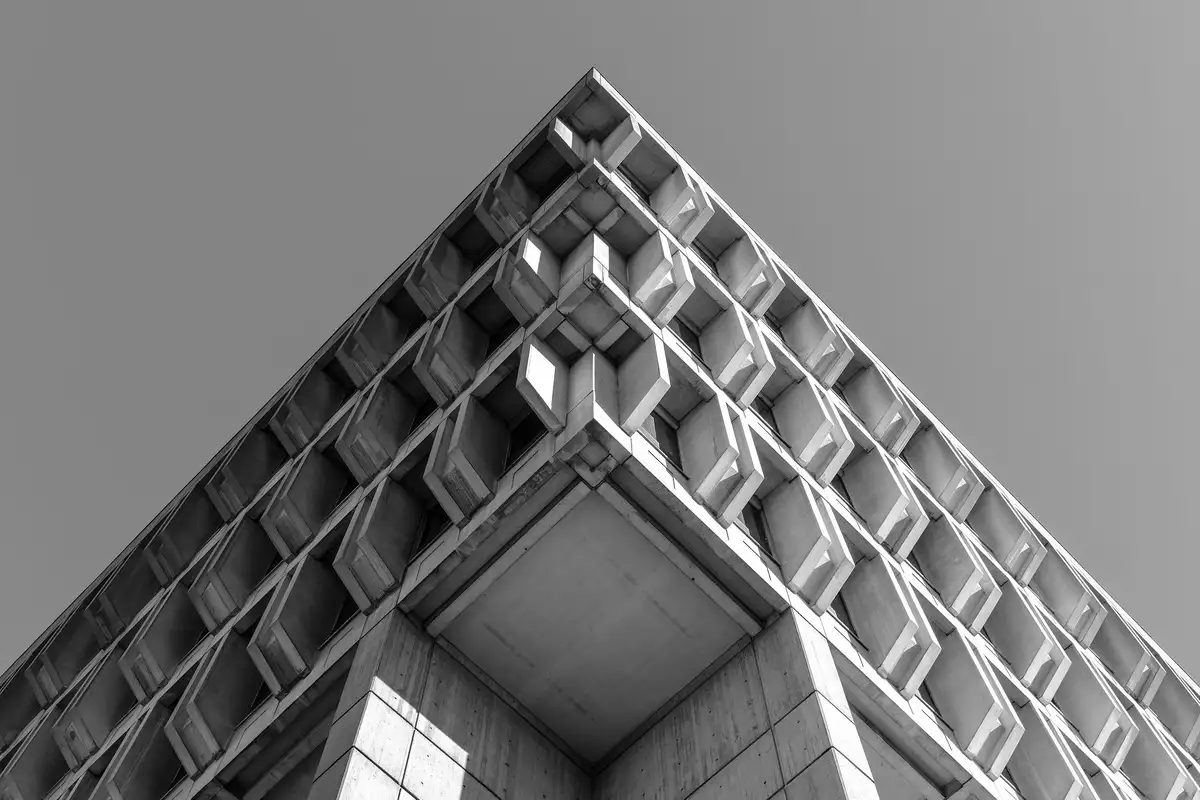 Low-angle view of a brutalist tower corner: deeply recessed modular window bays forming a symmetrical chevron against flat sky.